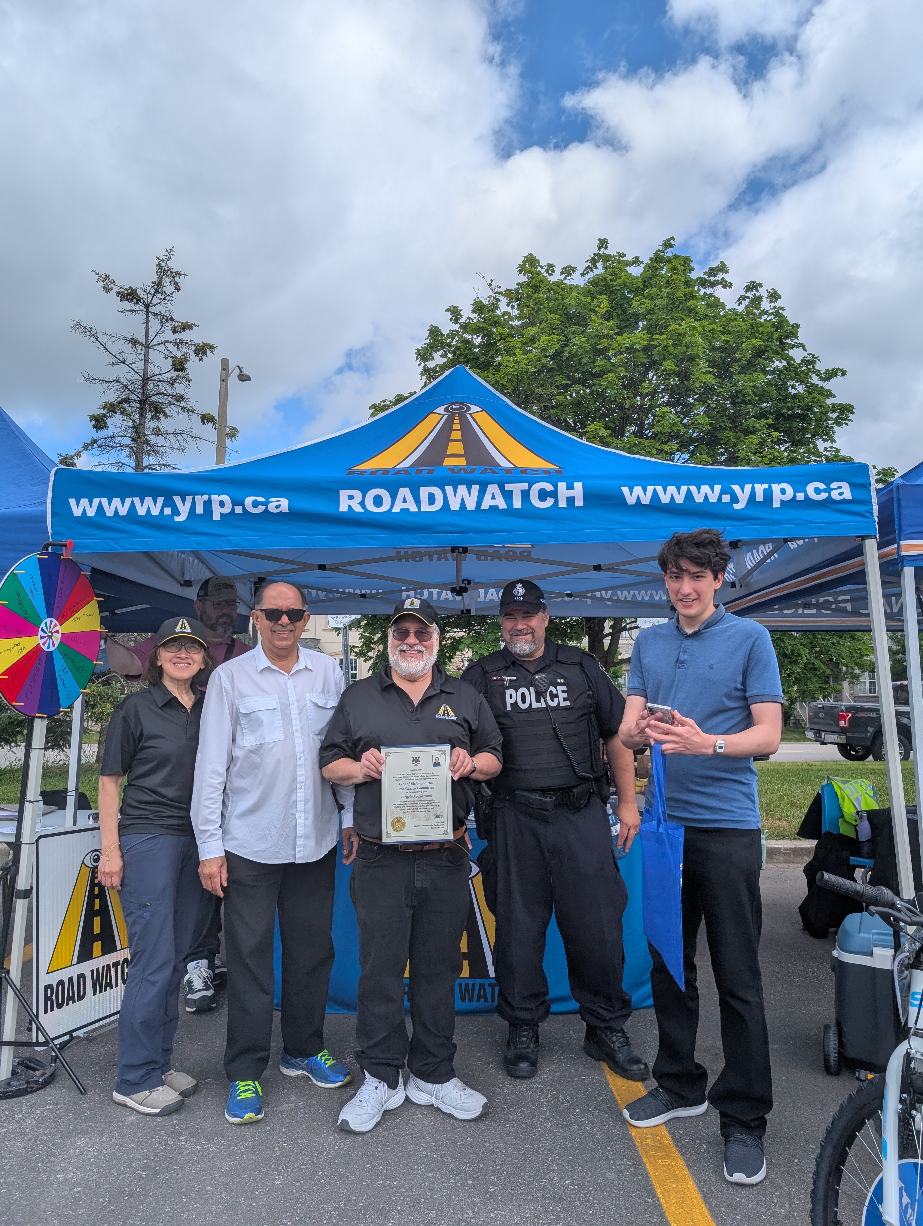 Marty Paulin holding a community appreciation certificate under the Road Watch tent